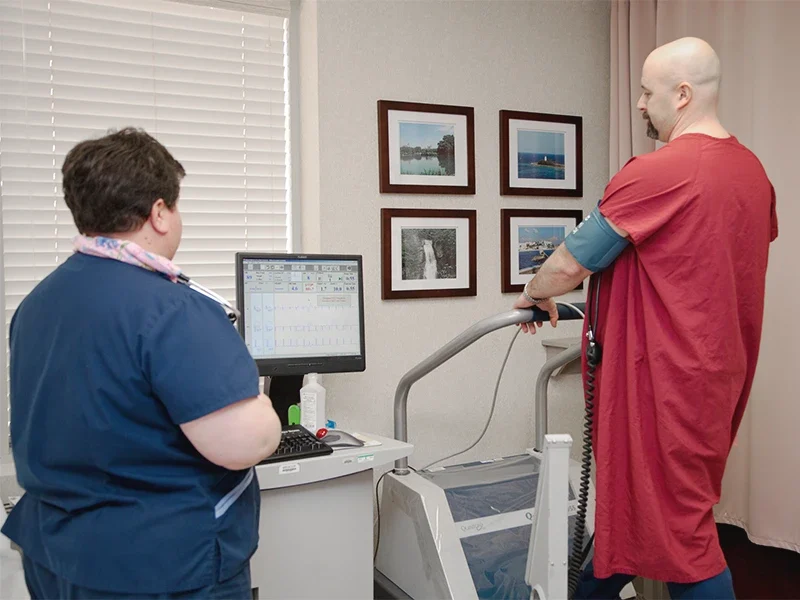 Patient undergoing cardiac stress test on treadmill with clinician monitoring heart activity