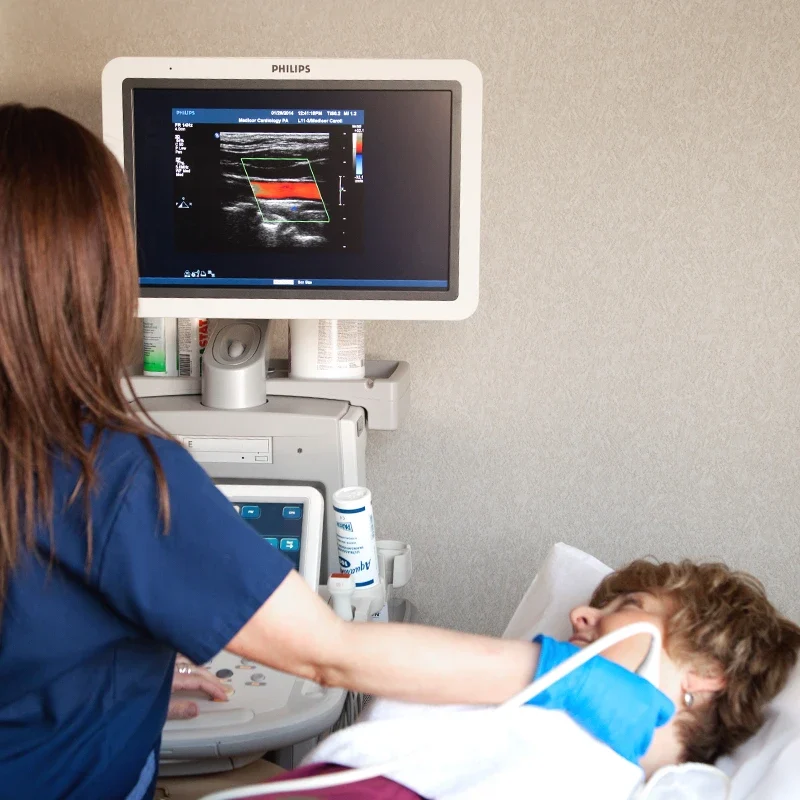 Technician performing vascular ultrasound imaging to assess blood flow in patient